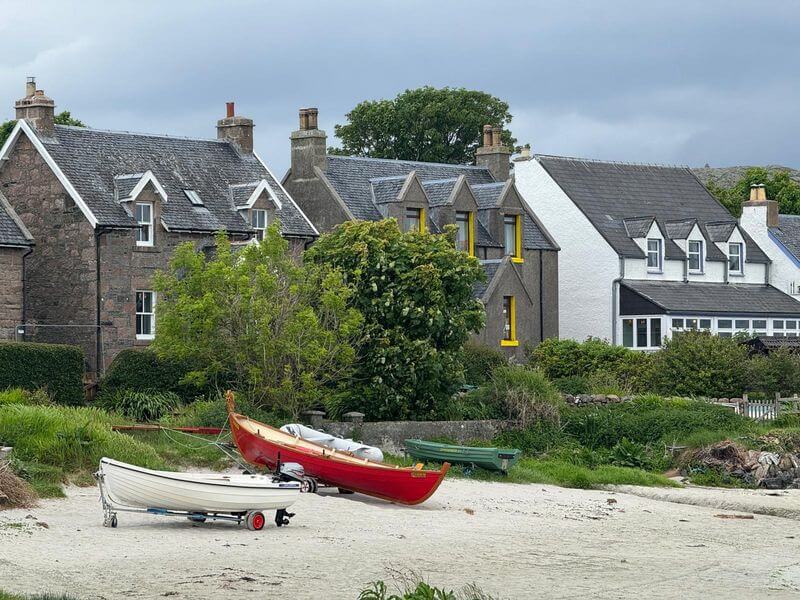 Deserted Scottish beach featuring small boats and quaint homes in background