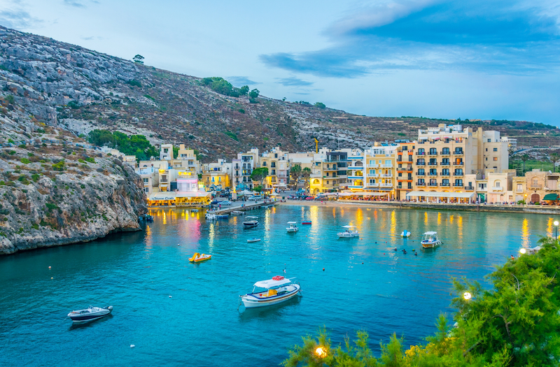 view of Xlendi Bay, Malta, in early evening with fishing boats and restaurants