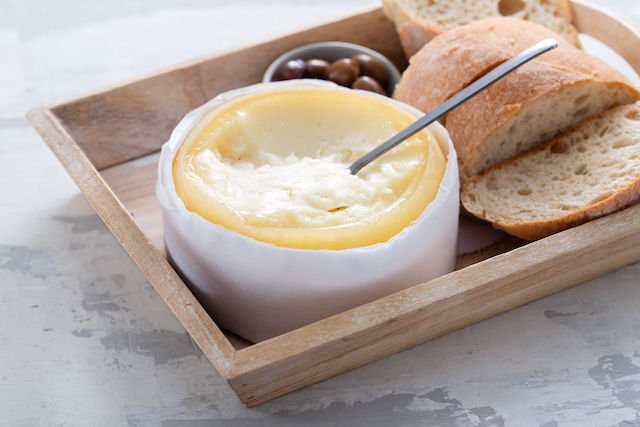 Serra da Estrela, Portuguese cheese, in a wooden tray accompanied by slices of white bread and a pot of black olives