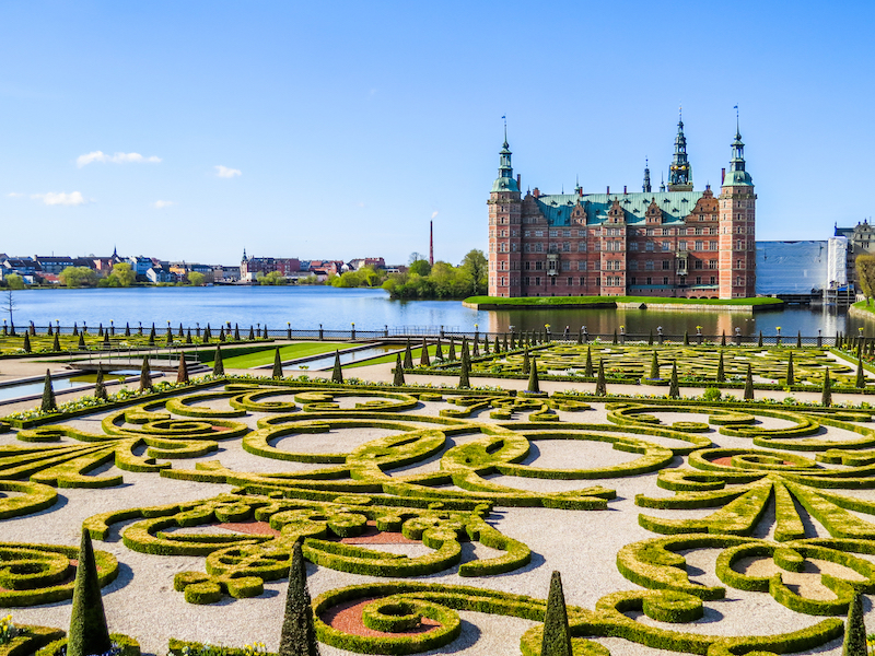 Frederiksborg Castle, Denmark, with its landscaped baroque garden in the foreground and a clear blue sky in the background