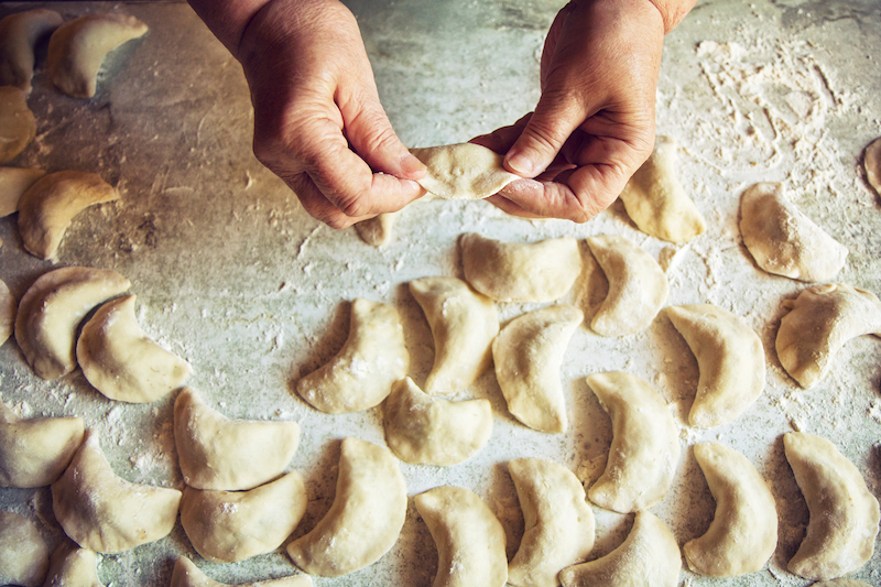 close up of a pair of hands making pierogi Polish dumplings on a floured surface