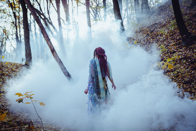 mystical scene showing a woman with long red hair walking through a cloud of mist in a forest