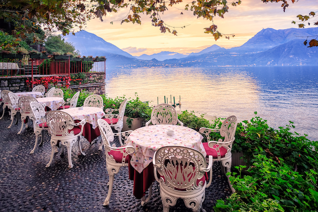 a terrace with a sunset view of Lake Como furnished with decorative white wrought iron chairs and tables