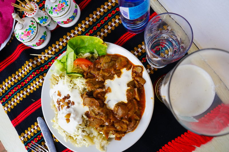 a plate of stew and drinks on a decorative tablecloth in the Hungarian village of Hollókő 