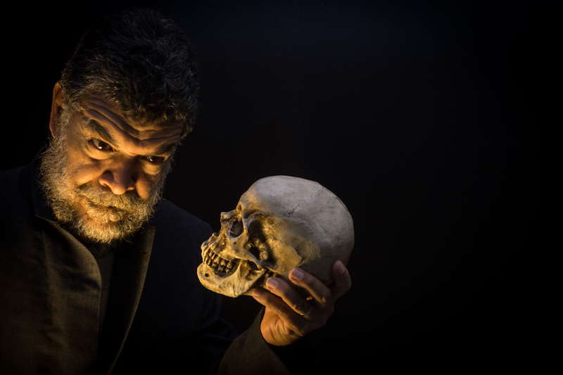 dramatically lit close up of a man playing Hamlet holding a skull, with a black background