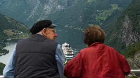 Two travellers look over a cruise ship sailing up Geiranger Fjord.