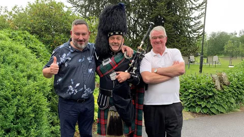 Two travellers taking a picture with a highland bagpipe player.