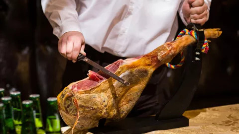 A man cutting off slices of iberian ham.