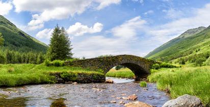 A view of a bridge spanning over a river leading into Loch Lomond in Scotland on a bright day.