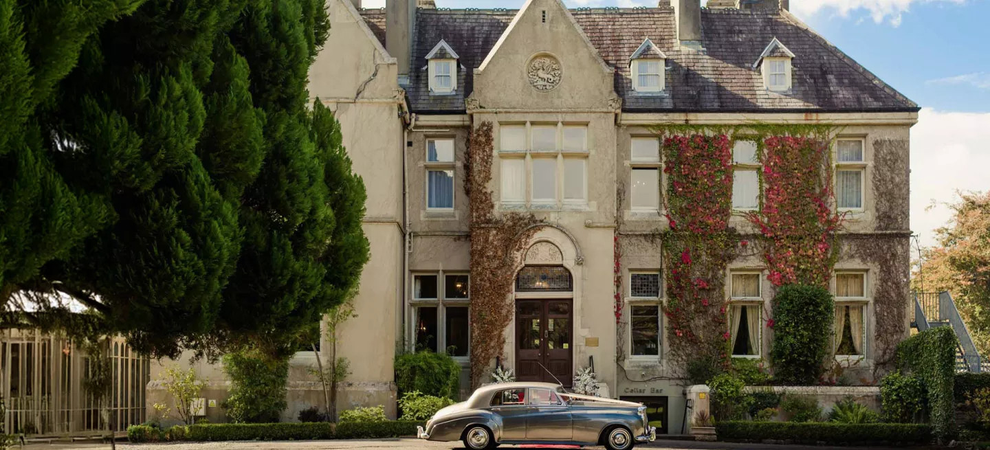 Historic ivy-covered hotel, with a vintage car parked in front.