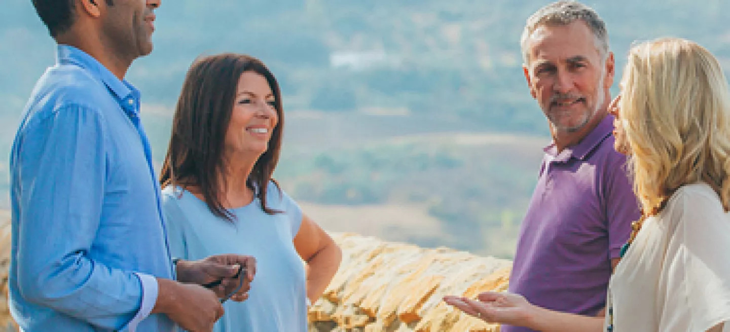 A group of four people chatting on a stone wall overlooking rolling hills in a countryside setting.