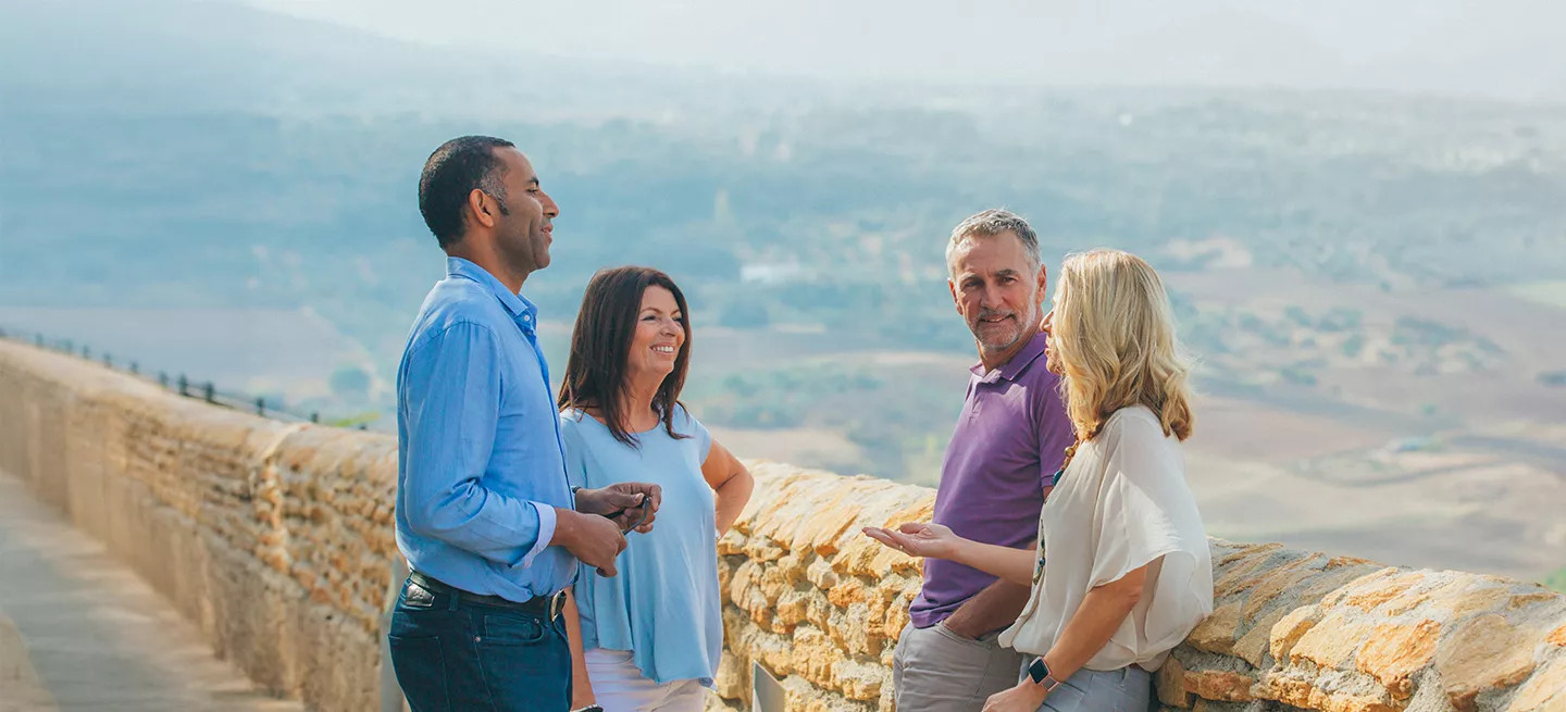 Group of four people chatting on a stone wall overlooking rolling hills in a countryside setting.