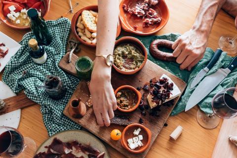 A spread of various Spanish tapas dishes with a woman and man's hand picking up various foods.